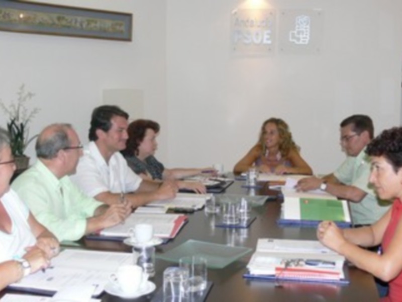 Reunión de trabajo en una sala de conferencias con personas sentadas alrededor de una mesa llena de documentos y vasos de agua.