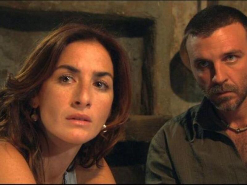 Dos personas en una escena dramática, posiblemente de una película o serie, en un entorno oscuro y antiguo.