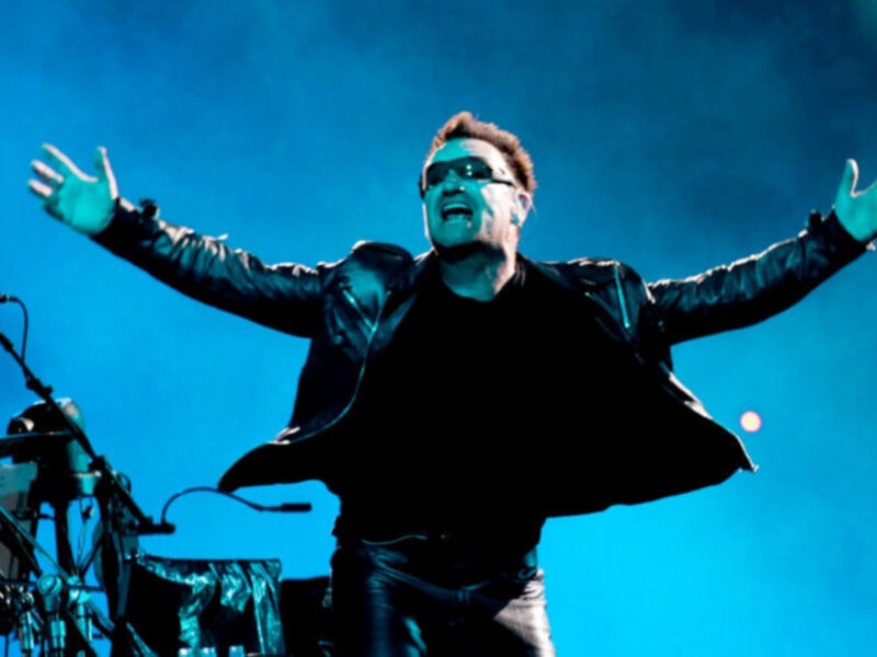 Artista en escenario con brazos levantados, iluminado con luz azul.