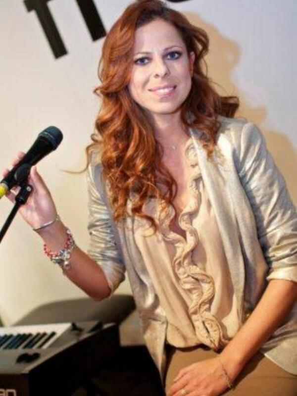 Persona con cabello largo rizado sosteniendo un micrófono en un evento público.