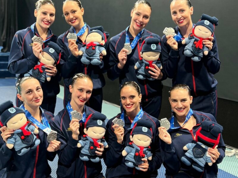 Equipo de natación sincronizada celebrando con medallas y peluches.